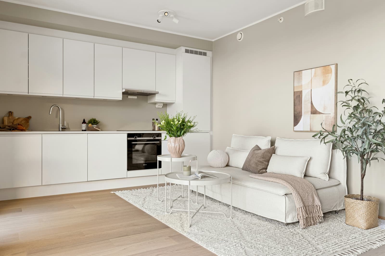 An open-plan condo living area painted in a warm greige, with light wood flooring and pale cabinetry